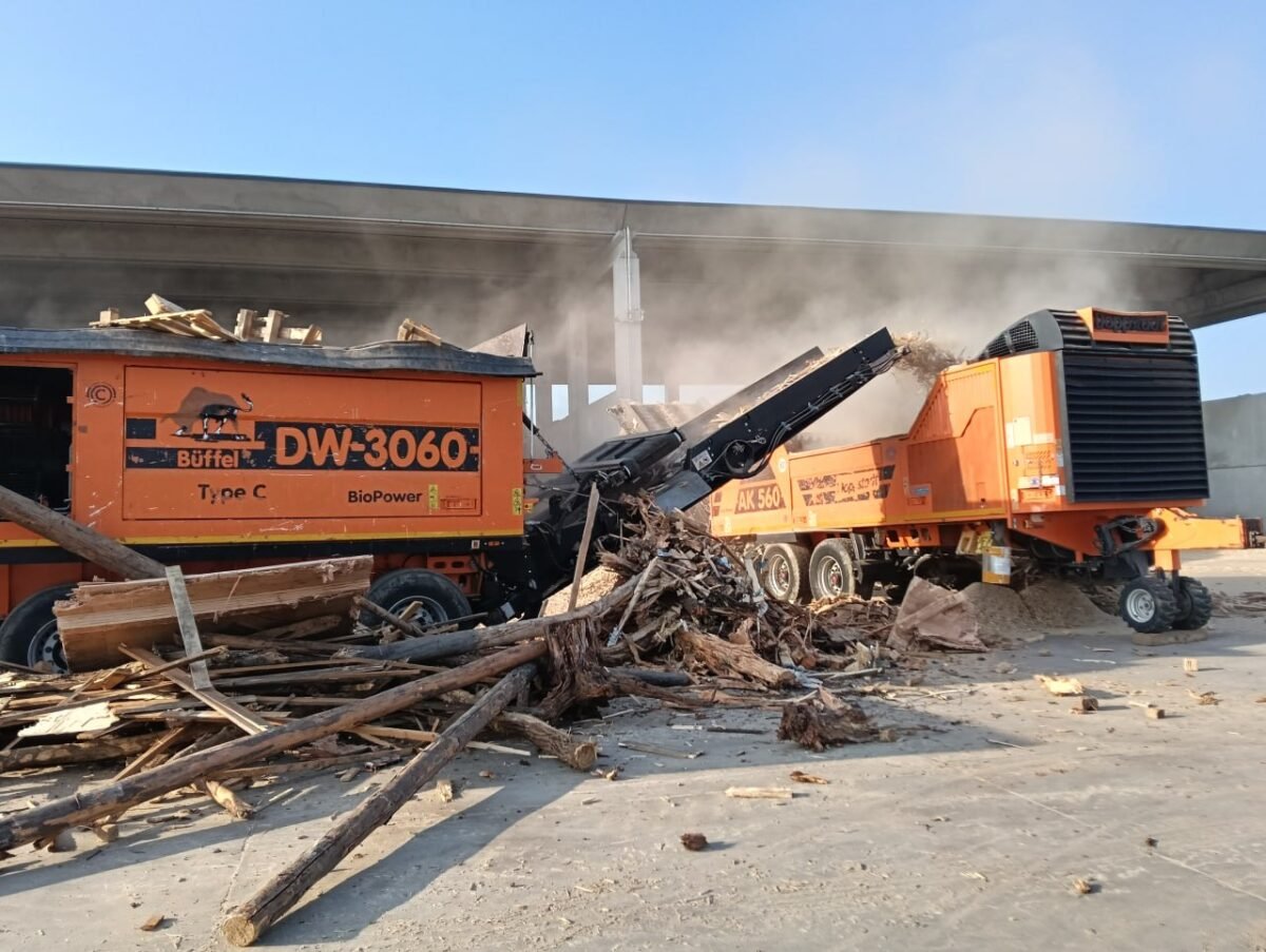 I due trituratori del legno al lavoro con la nuvola di polvere sopra l’impianto di riciclo